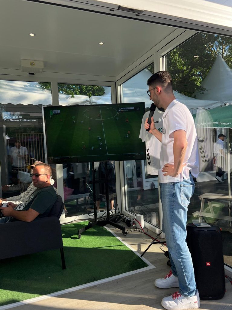 Hessentag AOK #16 Der Kommentator begleitet ein Livespiel in der eFußball-Arena im verglasten Container beim Hessentag im Auftrag der AOK.