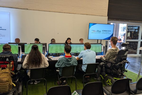 Eine vollbesetzte, inklusive Spielrunde mit zwei Rollstuhlfahrern in der eFußball-Arena des IFBA auf der REHACARE in Düsseldorf.
